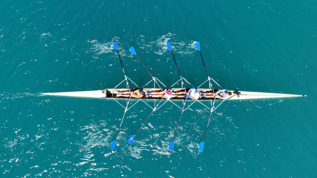  Aerial view of four rowers in a sport boat on emerald water | DXC Technology
