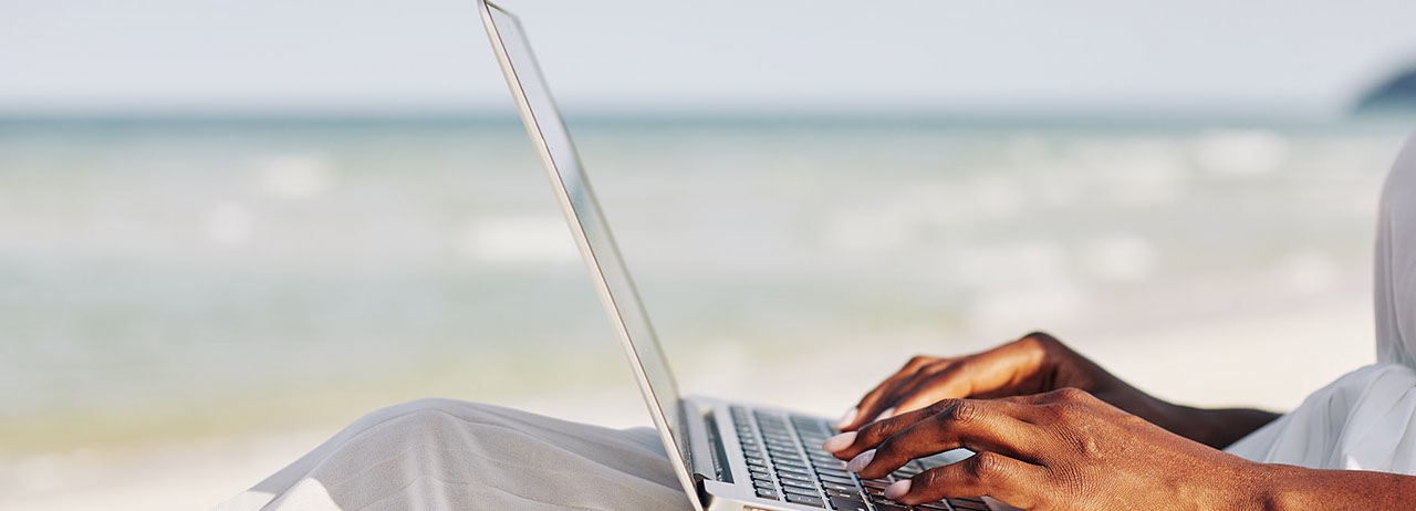 Side view of young woman sitting on beach and typing on laptop