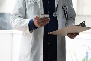 Doctor reviewing data on phone and patient chart; AI-powered app for Parkinson’s patients | DXC Technology Customer Story