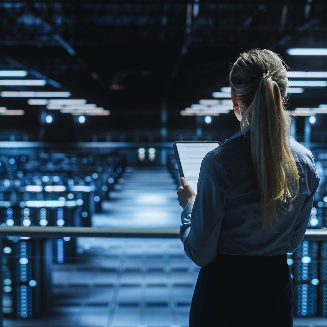 Female technician surveying a security datacenter while looking at a tablet, Security solutions | DXC Technology