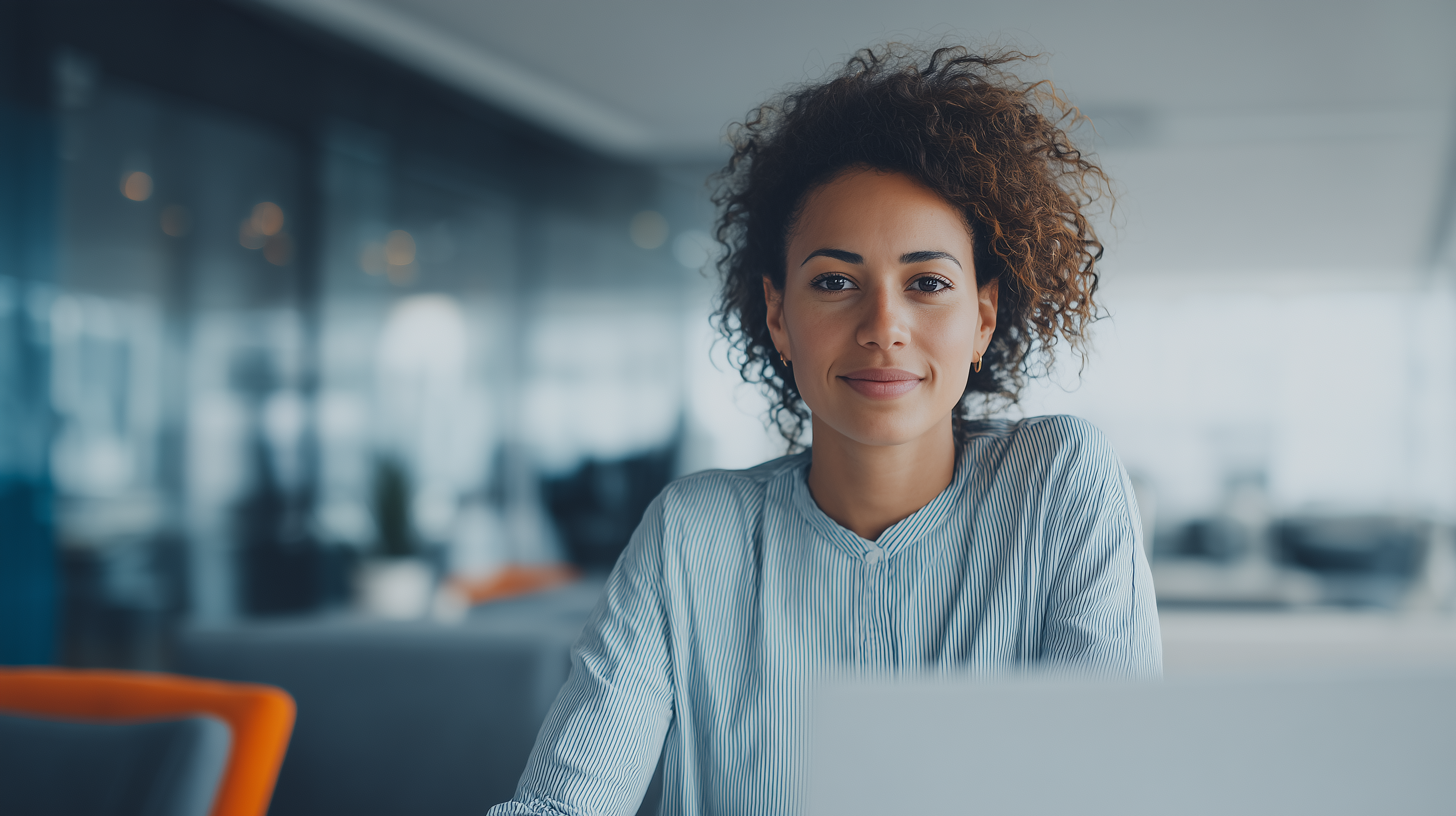 Smiling female worker sitting at a desk in open plan office, Enterprise Data & Intelligence | DXC Technology Solutions