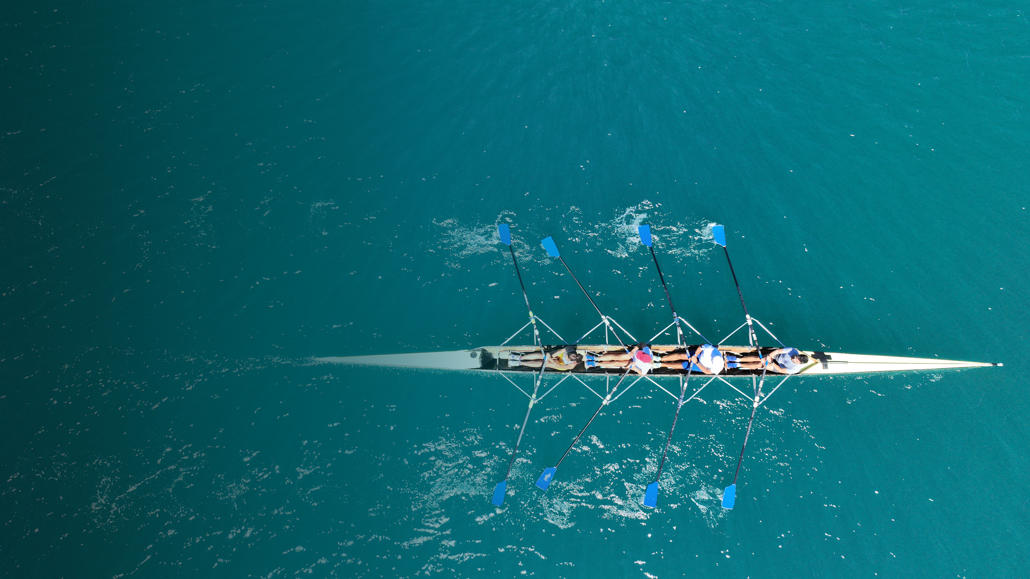 Aerial view of four rowers in a sport boat on emerald water | DXC Technology Campaign 