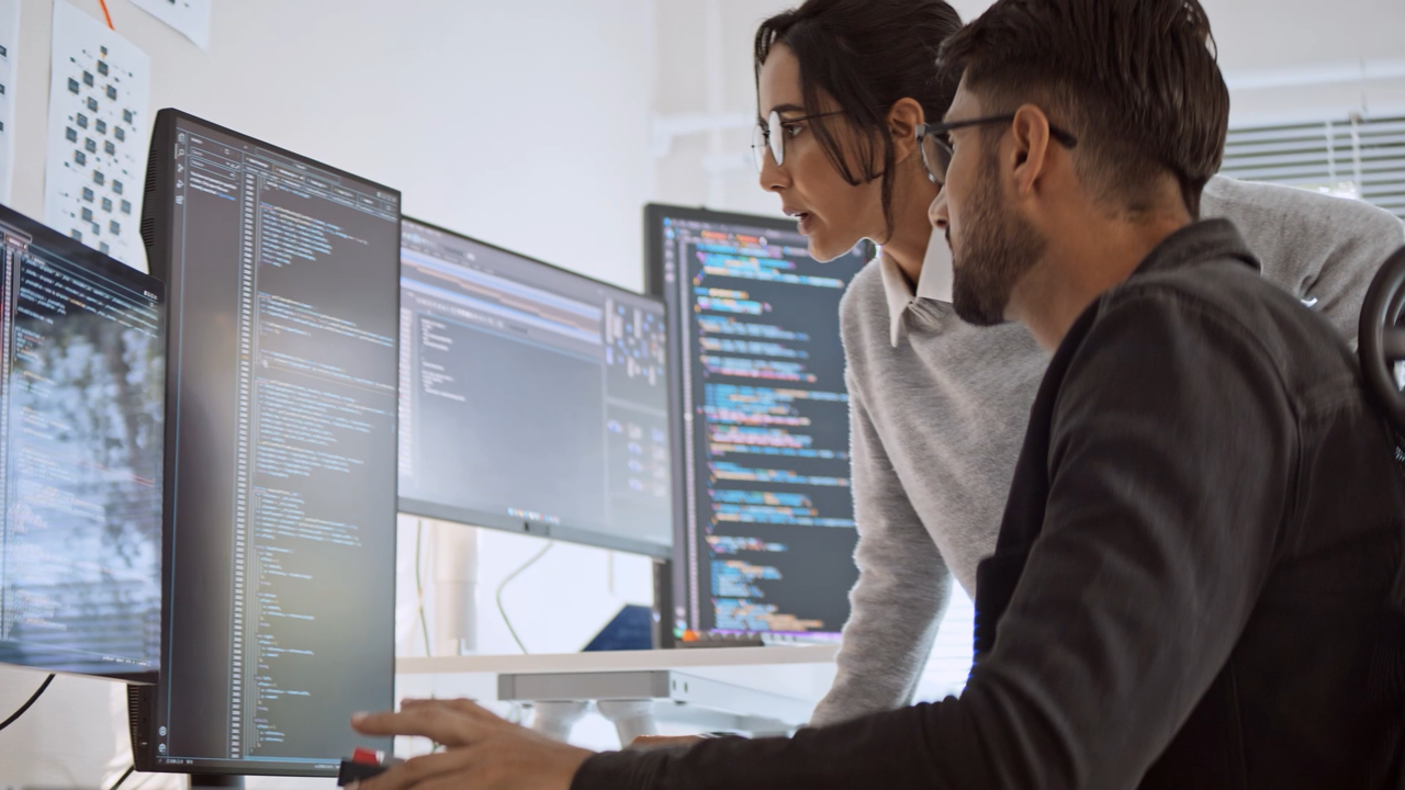 Male and female programmers looking at code on a screen, Fast RISE with SAP | DXC Technology