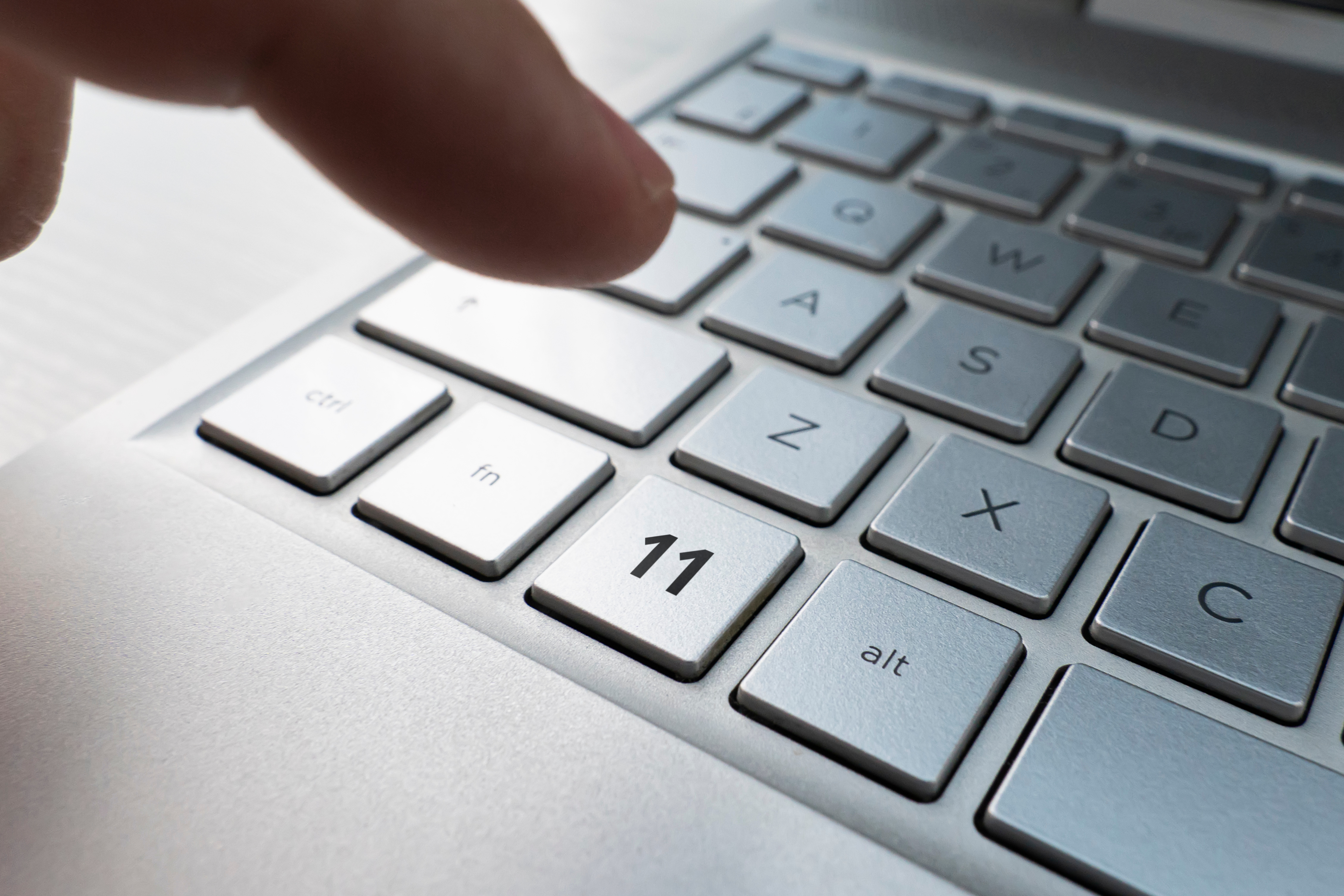 a person pressing a keyboard button labeled "11," representing Windows 11 upgrade| DXC Technology 
