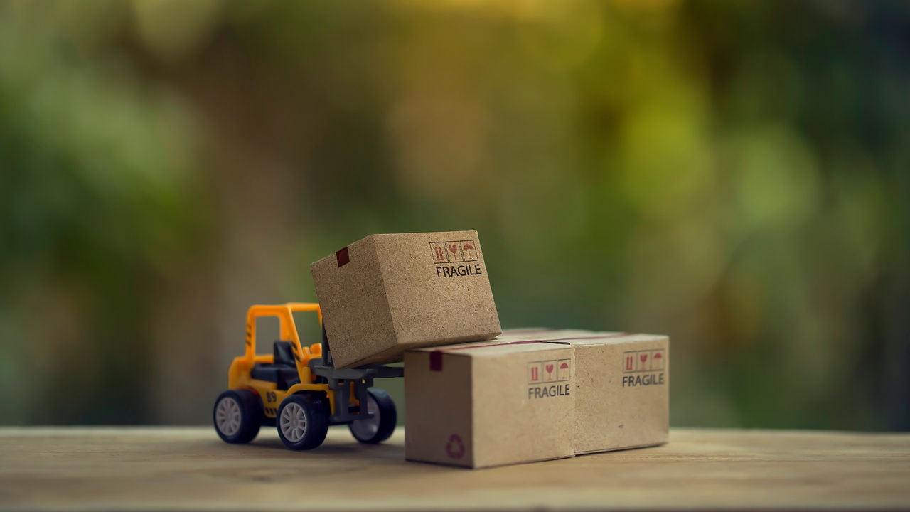 Logistic and cargo freight concept: Fork-lift a truck moves a paper box on table. depicts International freight or shipping service for online shopping.
