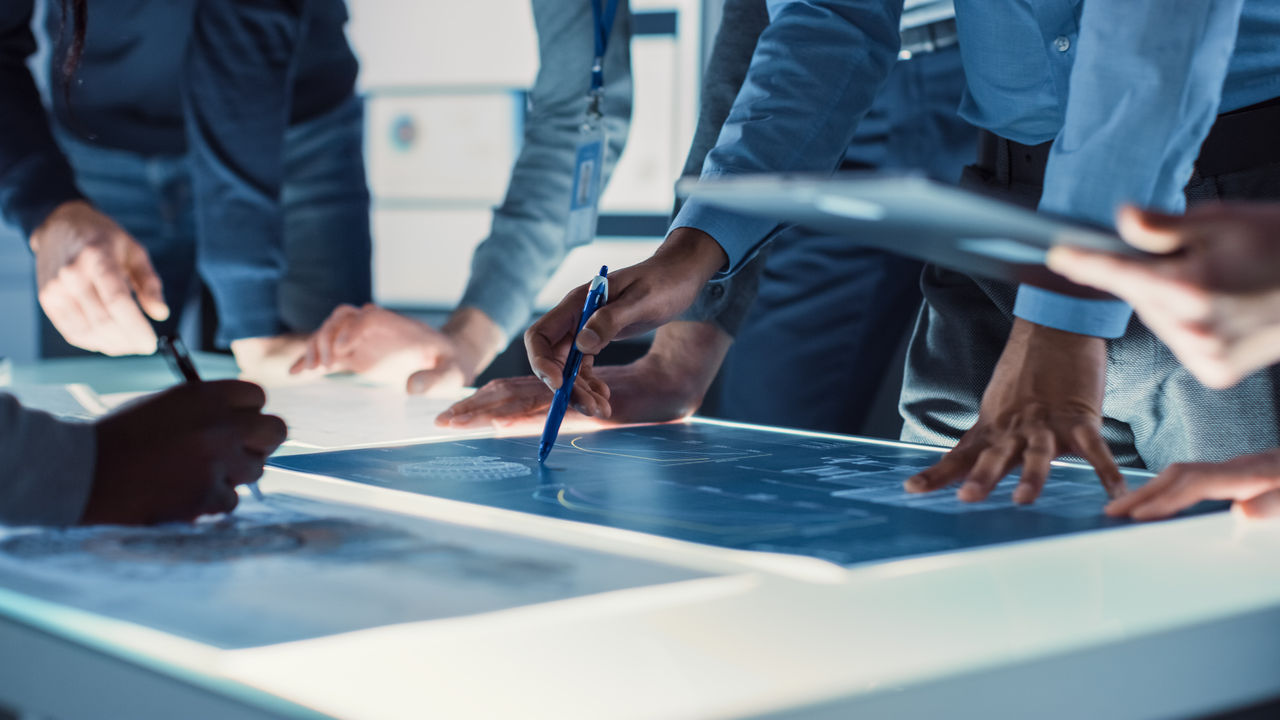 Group of people around a worktable, handling charts | DXC Technology
